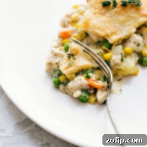 Savory and flavorful chicken pot pie on a plate, with a bite taken out to reveal its creamy center.