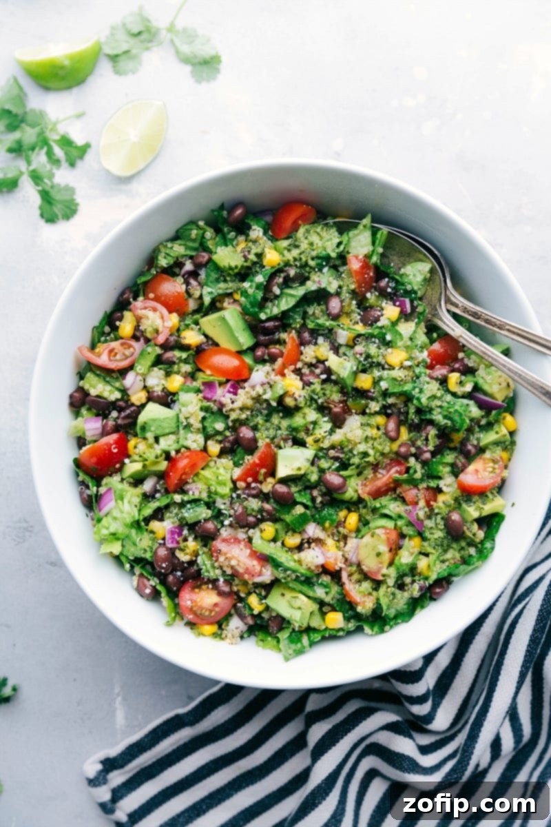 A vibrant bowl filled with Southwest Quinoa Salad, featuring quinoa, black beans, corn, tomatoes, avocado, and a rich dressing, with two serving spoons.