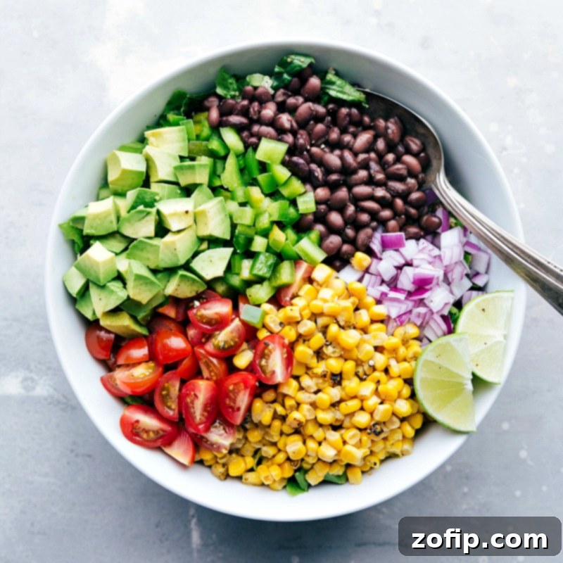 Fresh ingredients like black beans, charred corn, chopped onions, and tomatoes being added to a bowl of cooked quinoa and crisp lettuce for the salad.