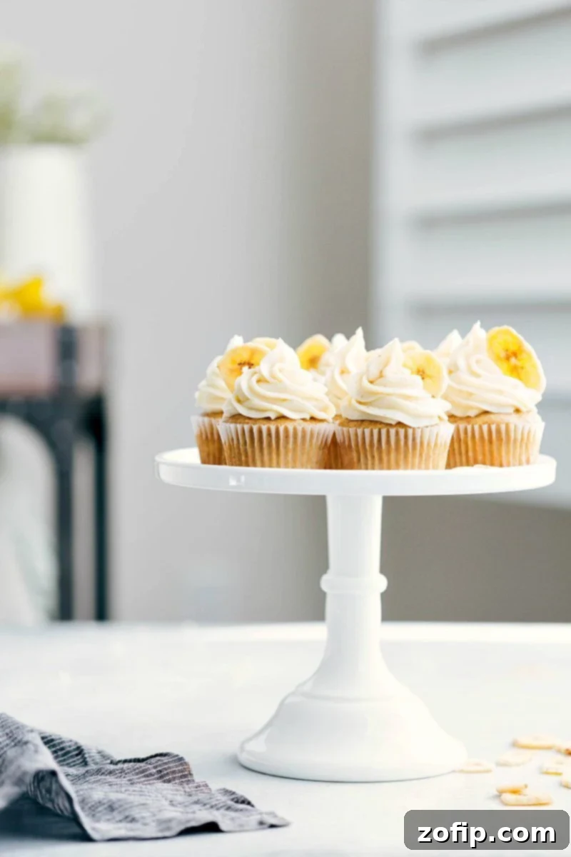 A stunning display of eight beautifully frosted Banana Cupcakes arranged on an elegant cake stand, showcasing their golden-brown hue and creamy white frosting, hinting at their delicious flavor.