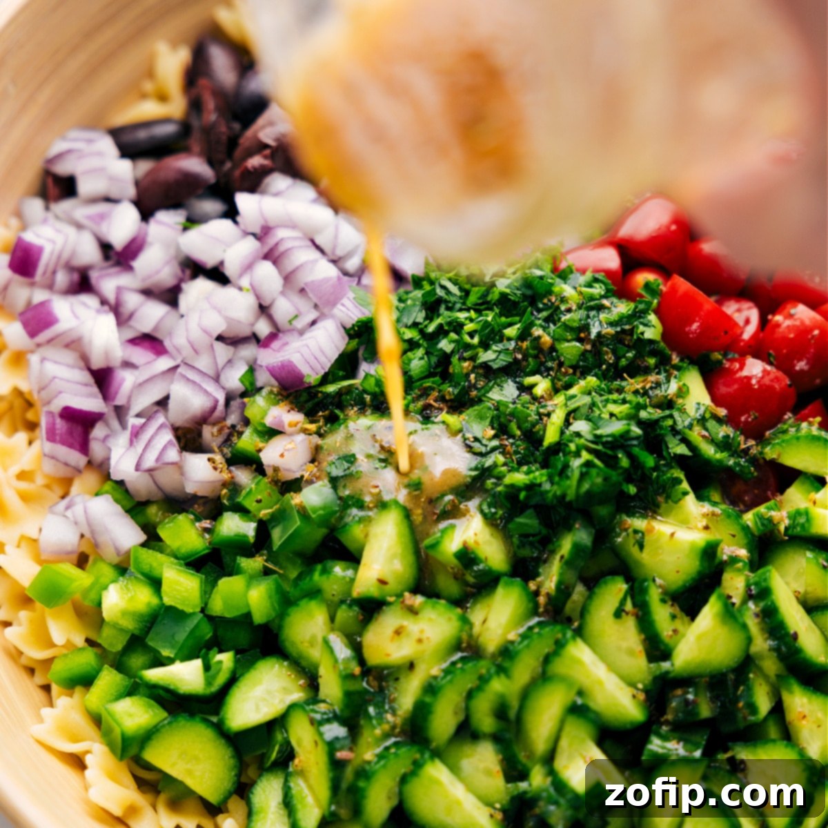 The vibrant Greek Dressing being poured over the freshly assembled Greek Pasta Salad.