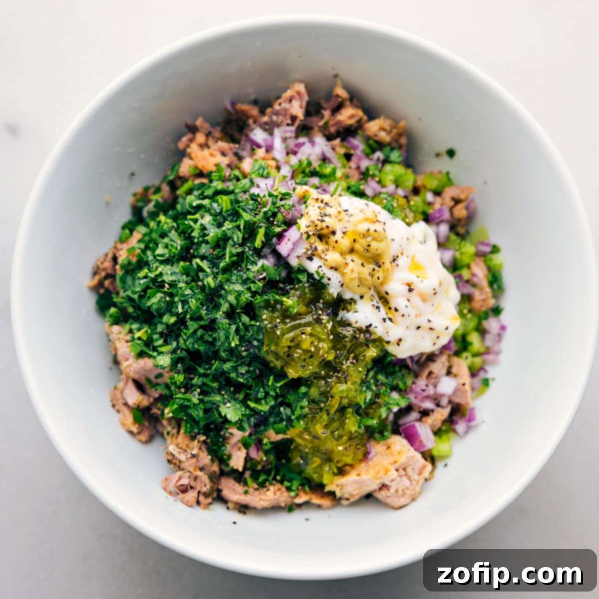 The absolute best tuna salad, freshly made and served in a elegant white bowl, garnished with a sprinkle of fresh parsley.