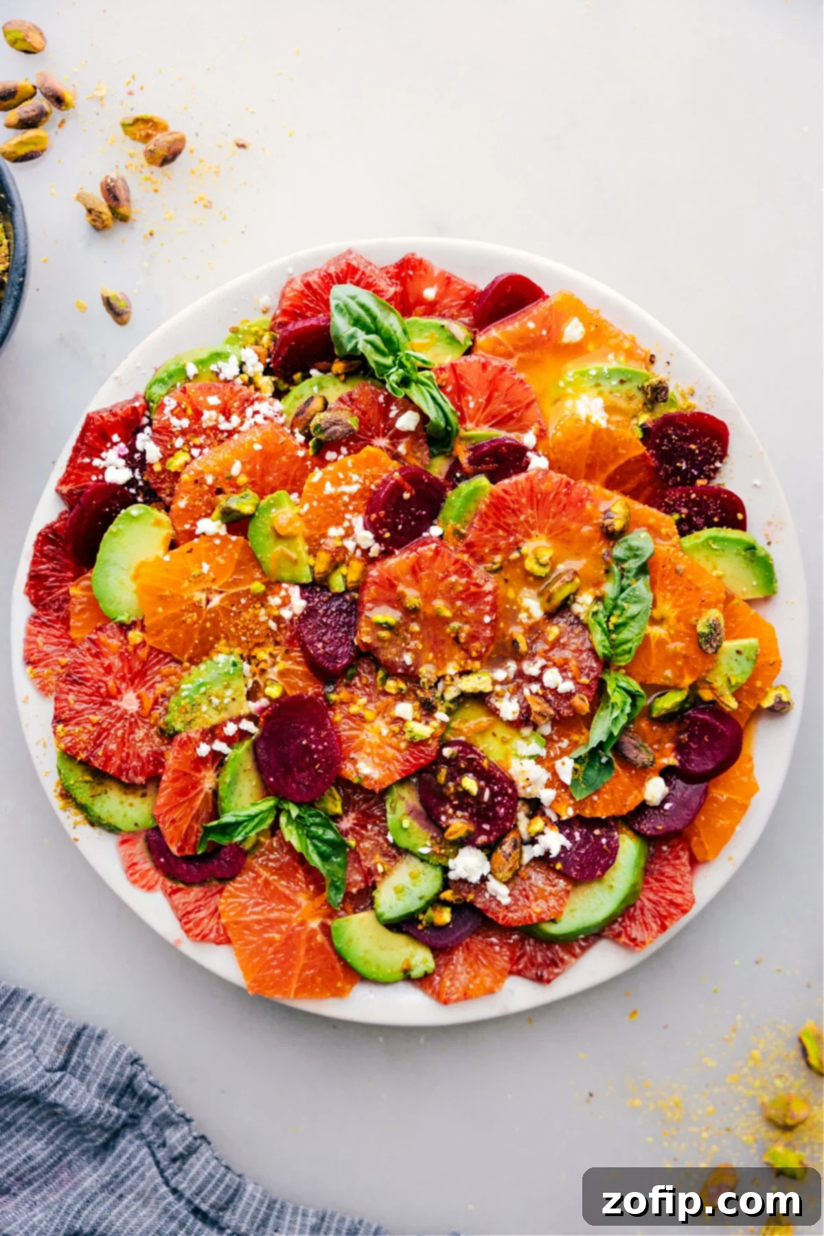 A large platter generously filled with vibrant citrus salad, featuring slices of various oranges, grapefruit, and avocado, garnished with pistachios and herbs, ready to be served at a gathering.