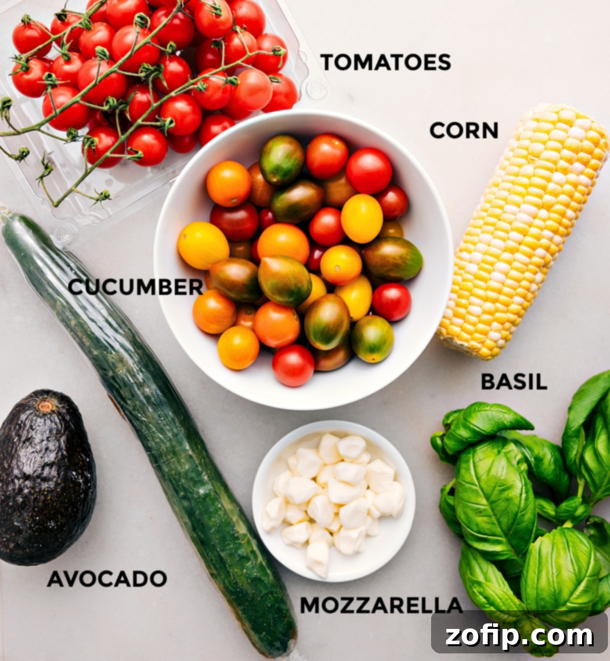 All the ingredients for this Panzanella recipe are prepped for easy assembly, including the tomatoes, corn, cucumber, basil, mozzarella, and avocado. Fresh and colorful produce.