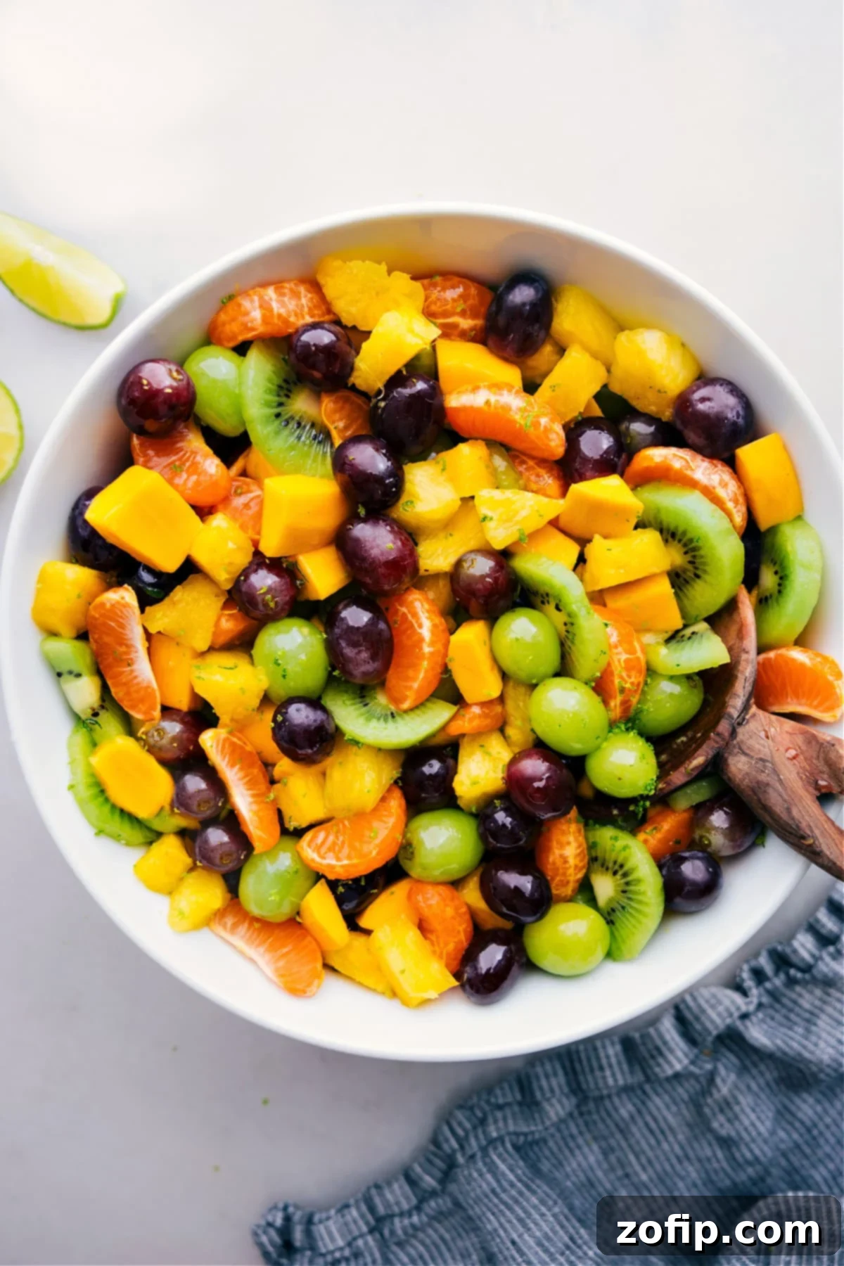 Refreshing Tropical Fruit Salad with Honey-Lime Dressing A large, vibrant bowl of freshly prepared Tropical Fruit Salad, brimming with colorful chunks of mango, kiwi, pineapple, and grapes, glistening with honey-lime dressing, photographed from a slightly elevated angle.