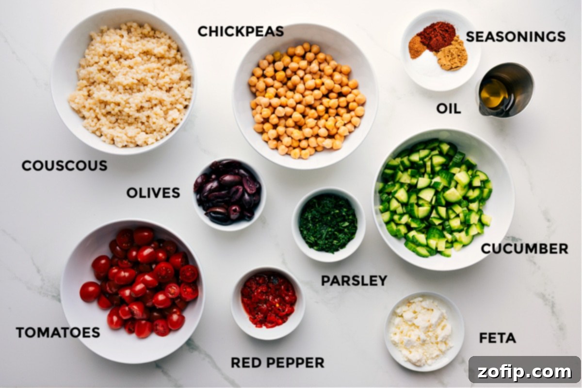 All the fresh ingredients prepped and arranged for easy assembly of the chickpea salad, including roasted chickpeas, pearled couscous, vibrant cucumbers, parsley, creamy feta, colorful bell peppers, juicy tomatoes, and briny olives.