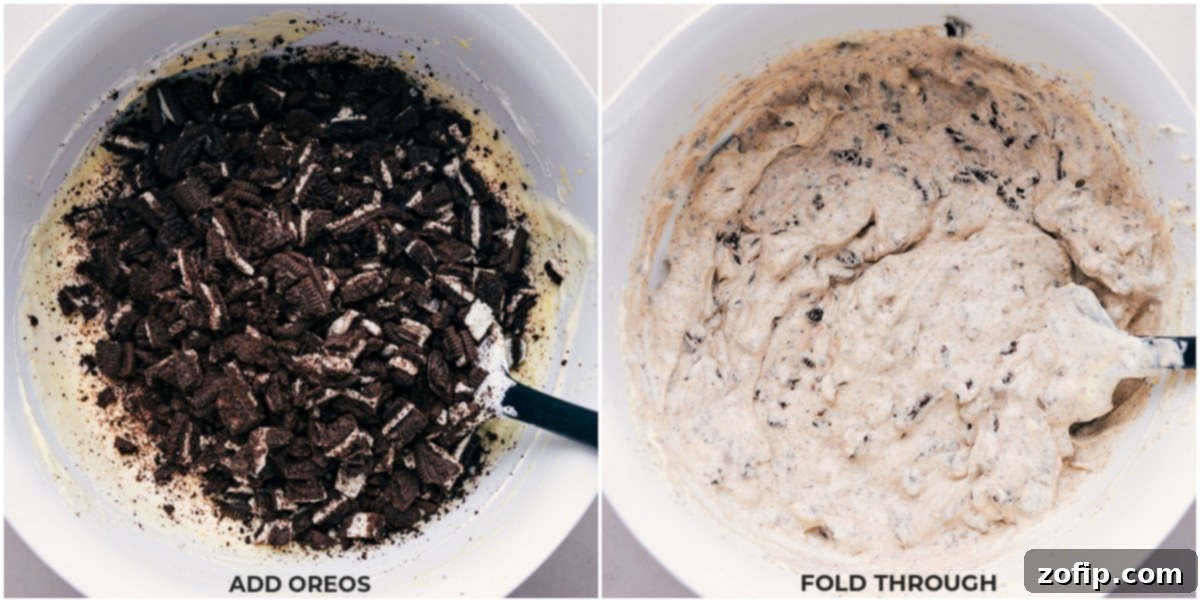 Crushed Oreos being gently added to the creamy fluff mixture and folded in with a spatula.