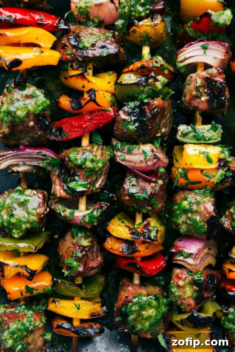 A plate of perfectly grilled steak kebabs, hot off the grill and enhanced with fresh basil sauce. Freshly grilled steak kebabs and vegetables on a serving platter, beautifully topped with basil sauce.