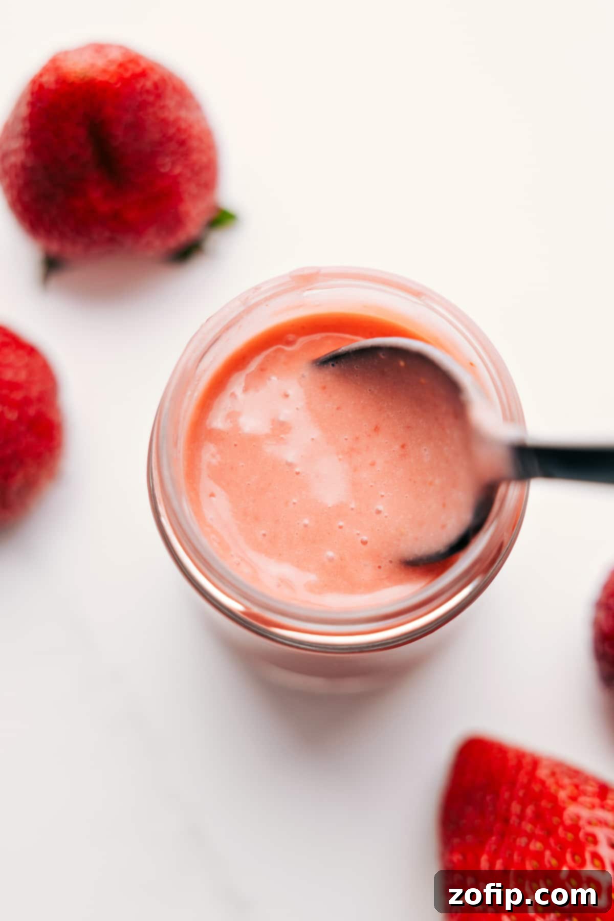 Luminous homemade Strawberry Vinaigrette in a mason jar, with a spoon gently scooping it, ready to be drizzled over a fresh salad. Focus on the vibrant red color and smooth texture.