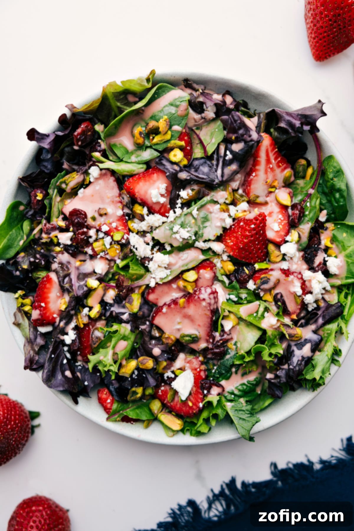 A vibrant, fresh salad generously tossed and drizzled with the homemade Strawberry Balsamic Vinaigrette, showcasing fresh berries, peaches, nuts, and creamy cheese on a bed of greens. Perfect for a summer meal.