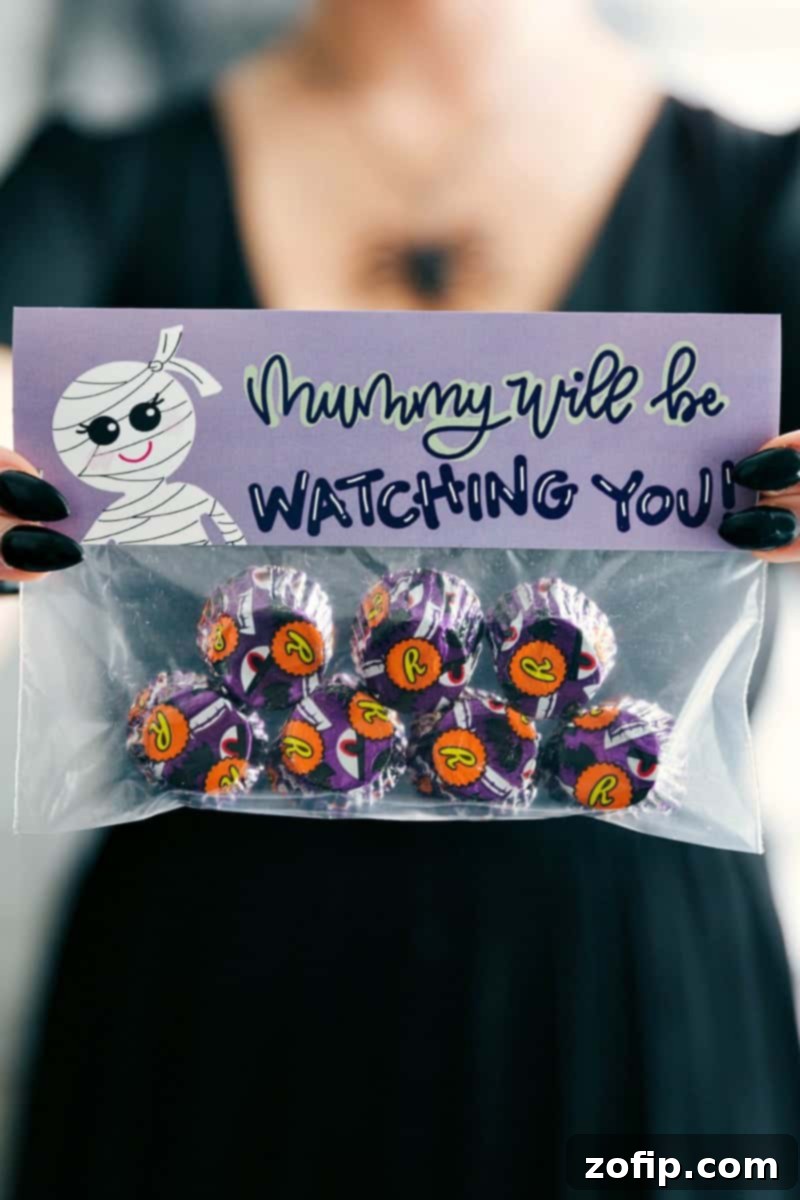 A hauntingly fun 'Mummy Will Be Watching You' Halloween treat bag with a mummy face topper, filled with candy eyeballs or eyeball-wrapped Reese's cups.