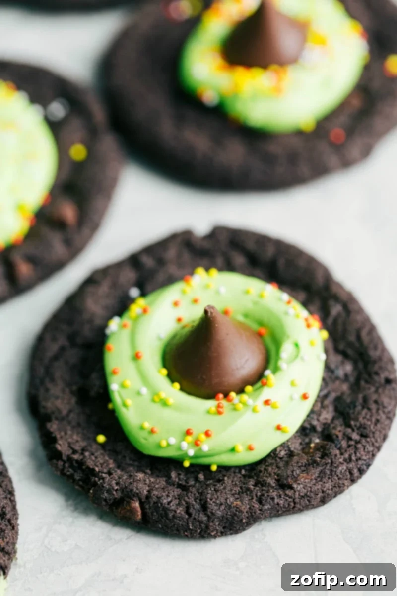 Halloween cookies decorated to look like a witch's hat, with dark cookie base, green frosting, and a chocolate kiss.