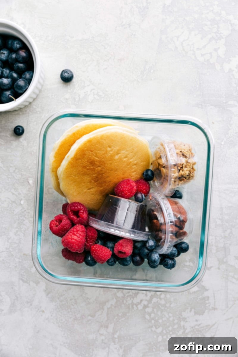 Packed Pancake Lunch for Kids Pancakes, syrup, granola, nuts, and fruit packed in containers, ready to go for a wholesome kids school lunch.
