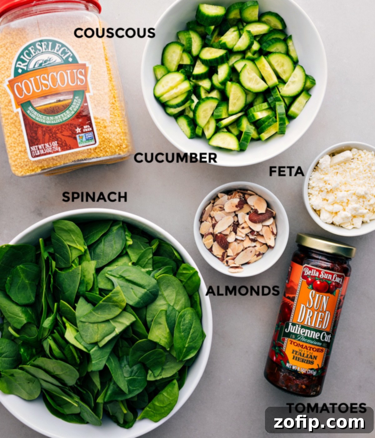 All the vibrant ingredients for Couscous Mediterranean Salad, including crisp cucumber, creamy feta, toasted almonds, juicy sun-dried tomatoes, fresh spinach, and fluffy couscous, neatly arranged and prepped for easy assembly.