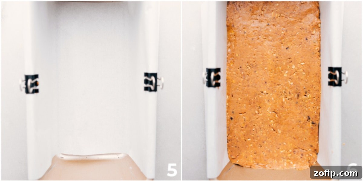 The protein bar recipe being pressed firmly and evenly into a bread pan lined with parchment paper, preparing for chilling.