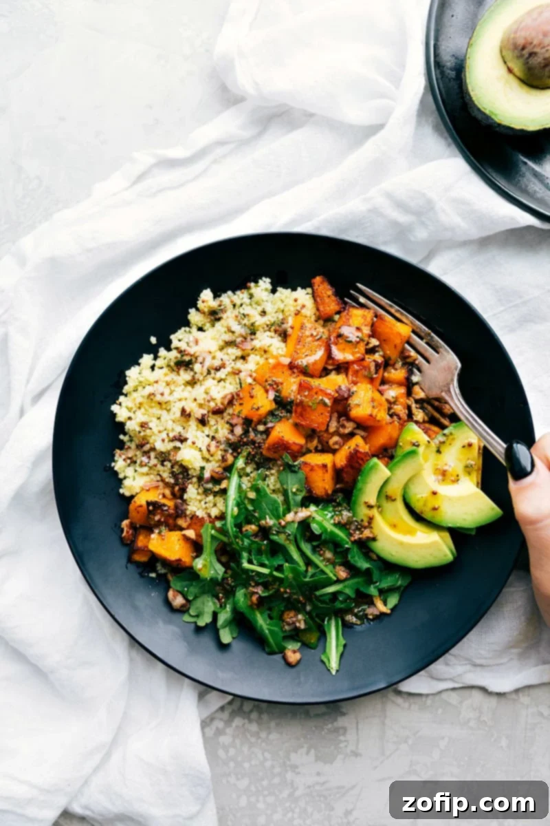 A beautifully plated butternut squash bowl featuring perfectly roasted butternut squash, fluffy couscous, fresh avocado slices, crunchy pecans, and a vibrant, flavorful dressing. This healthy fall meal is visually appealing and ready to eat.