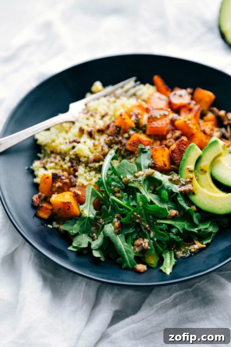 Close-up of a roasted butternut squash bowl, showcasing perfectly cooked couscous, golden-brown roasted butternut squash cubes, creamy avocado, and a generous drizzle of the signature dressing. A truly healthy and comforting Fall meal.