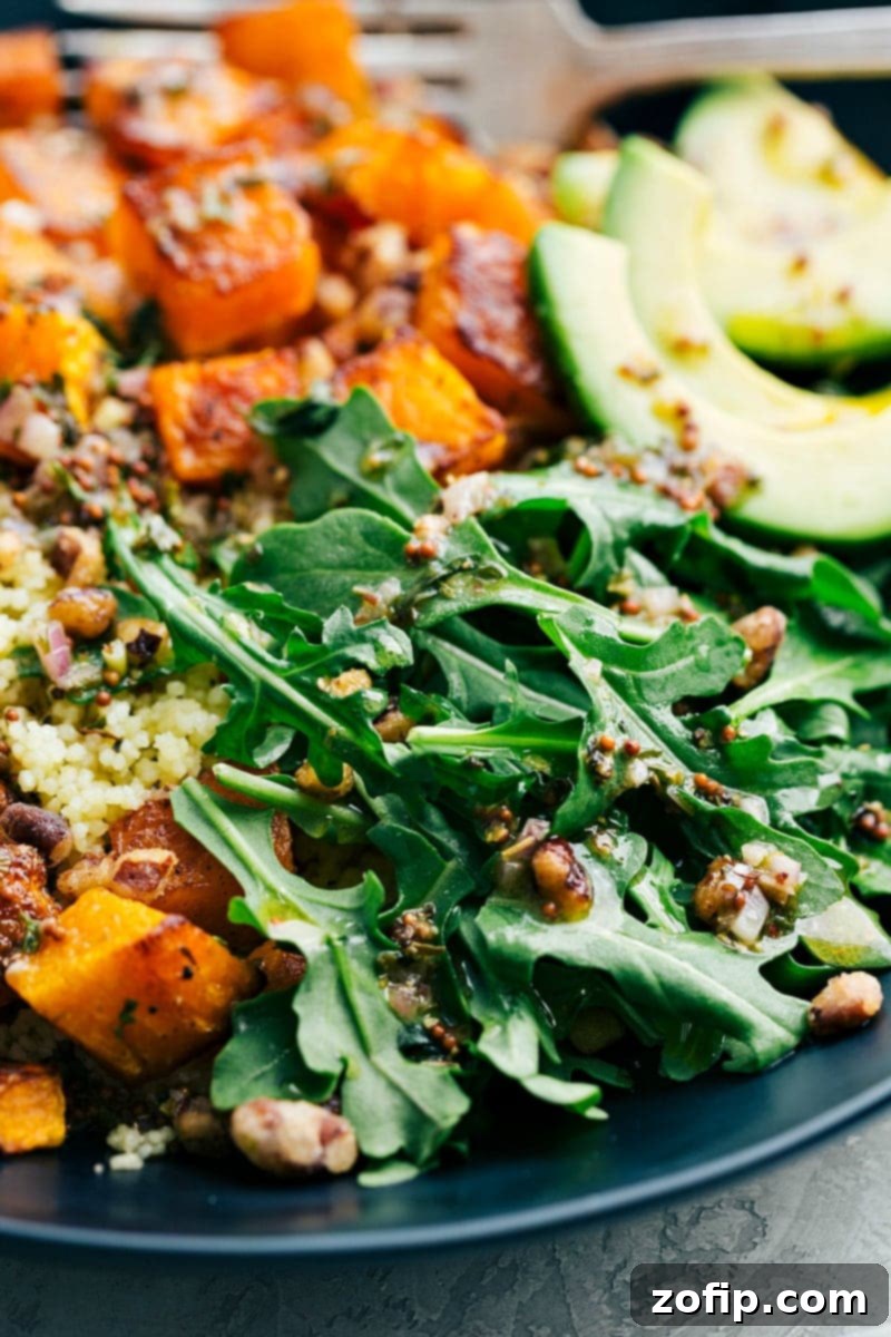 Overhead view of a prepared butternut squash bowl, showcasing a harmonious blend of roasted squash, couscous, avocado, and nuts. The fresh herbs and dressing add a vibrant touch.