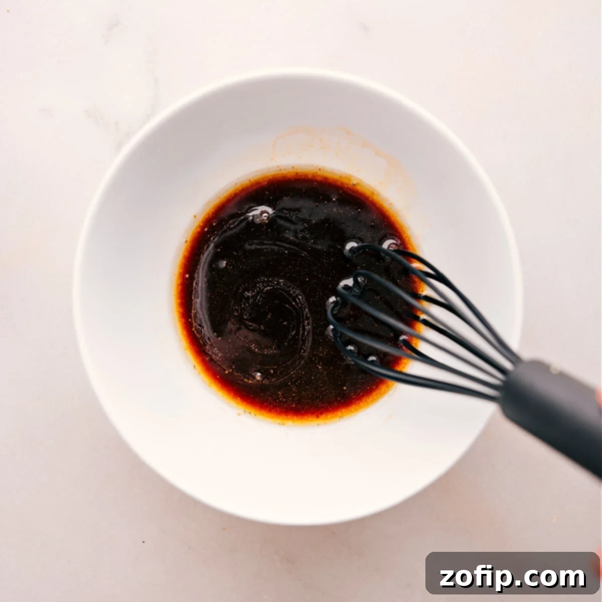 A hand whisking together the rich, savory stir-fry sauce in a small bowl, showcasing the blend of soy sauce, sesame oil, Sriracha, and brown sugar.