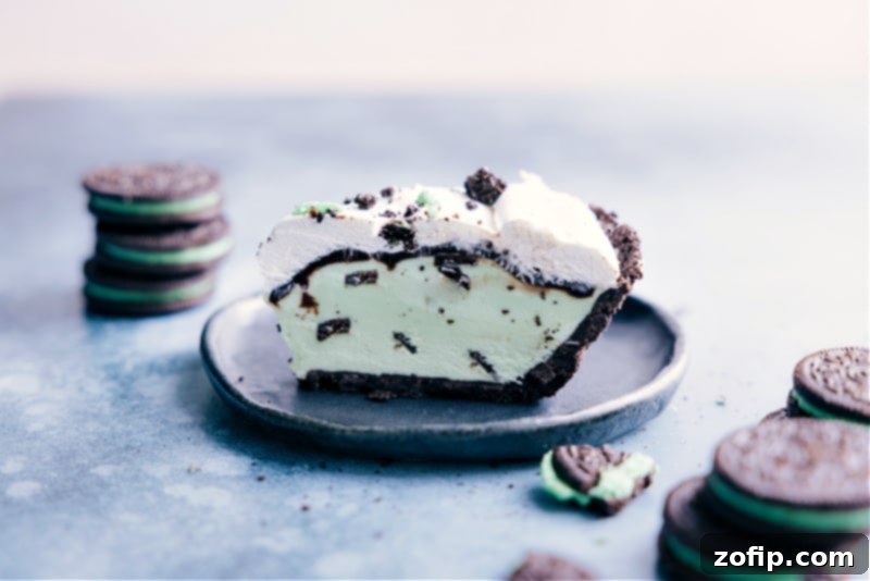 Grasshopper Pie -- the perfect summer treat that takes minutes to assemble! Recipe via ChelseasMessyApron #dessert #best #quick #easy #simple #oreo #icecream #treat #familyfriendly #kidfriendly #green #grasshopper #pie Side shot of a perfectly sliced Grasshopper Pie, showcasing its distinct layers of Oreo crust, mint ice cream, and whipped cream, ready to be enjoyed.
