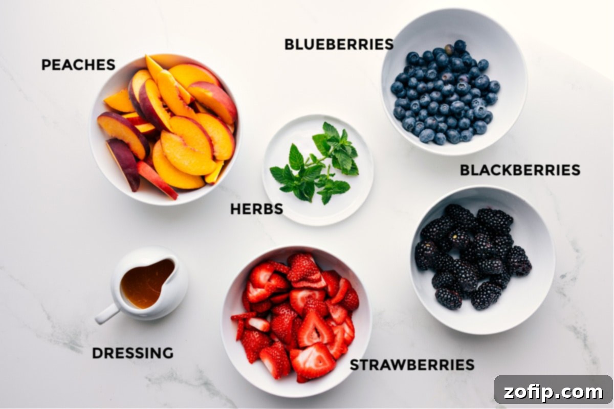 A curated display of fresh ingredients for Peach Fruit Salad, including whole peaches, an assortment of strawberries, blueberries, blackberries, and fresh mint, alongside components for the citrus dressing.