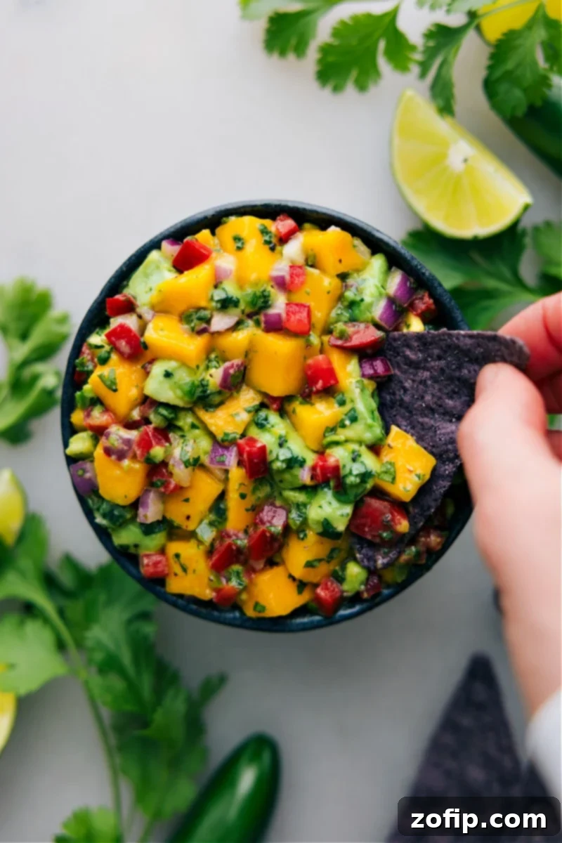 The Perfect Scoop: Enjoying Homemade Mango Salsa with Tortilla Chips An overhead shot showing a crispy tortilla chip scooping up a generous portion of fresh Mango Salsa, highlighting its vibrant colors and inviting texture