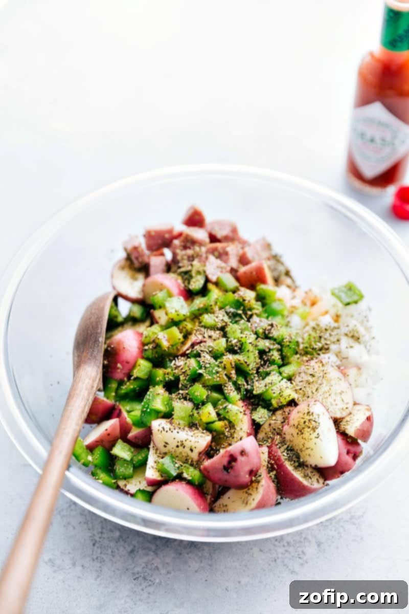 All the veggies, sausages, and seasonings added to a bowl to toss together.