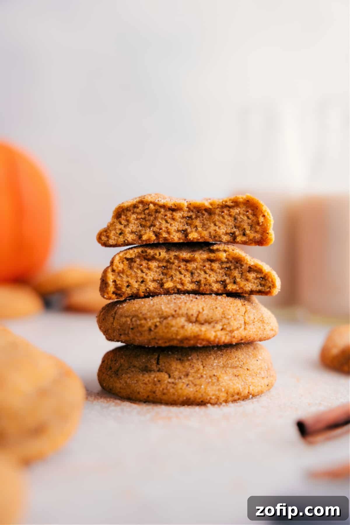 A stack of perfectly baked pumpkin snickerdoodles, with one cookie thoughtfully broken open to reveal its incredibly soft, moist, and chewy interior.
