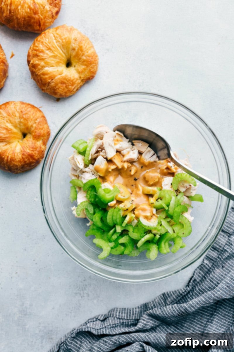 Overhead shot of a vibrant Honey Mustard Chicken Salad mixture in a bowl, ready to be assembled, with fresh croissants beside it.