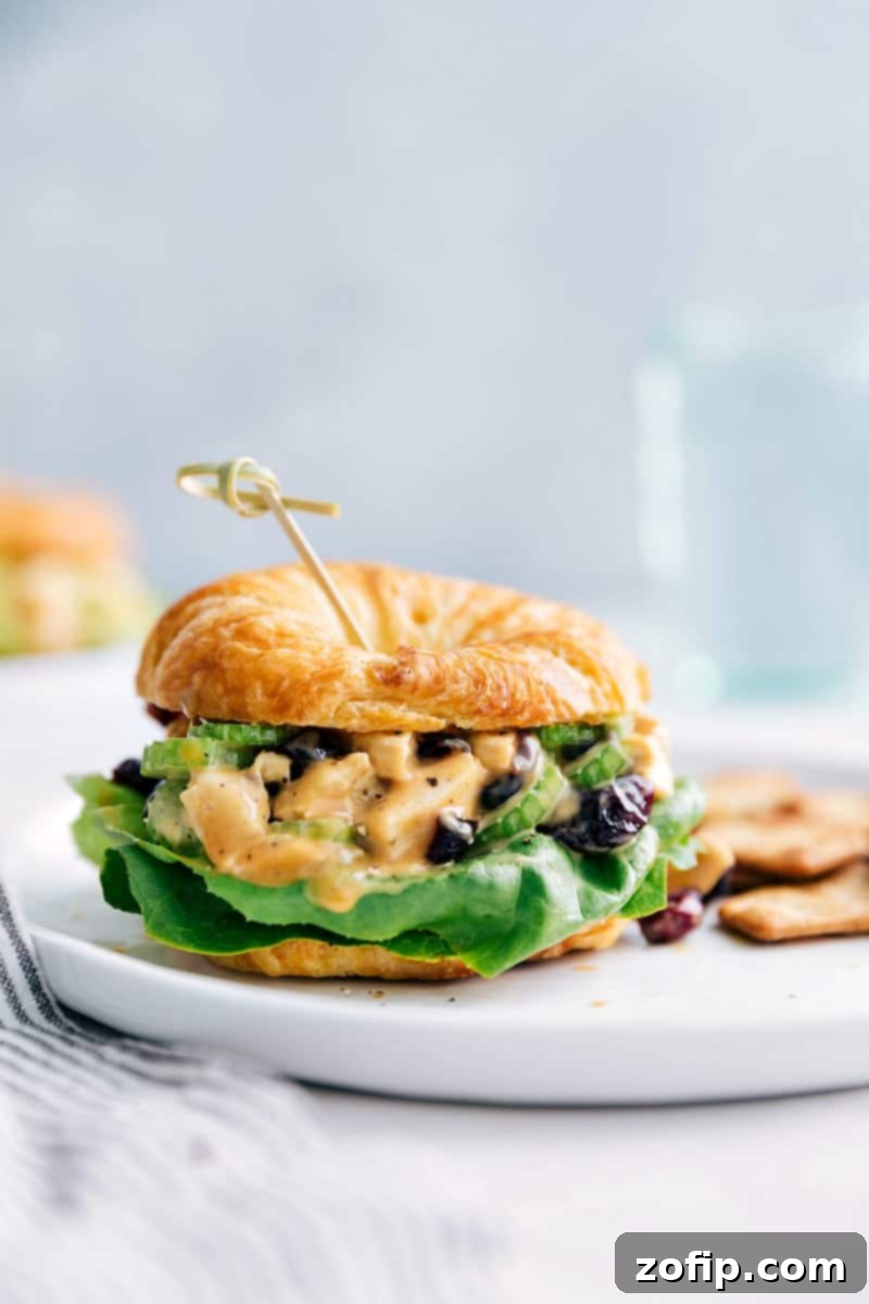 Close-up view of a beautifully assembled Honey Mustard Chicken Salad Sandwich, served with crispy crackers and a refreshing glass of water in the background.