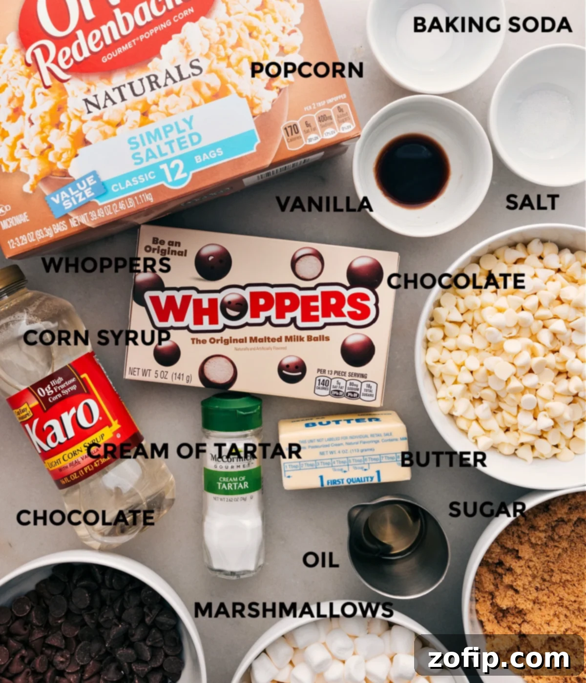 All the ingredients for gourmet chocolate popcorn are laid out: baking soda, salt, vanilla extract, plain popcorn, Whoppers, various chocolate chips, cream of tartar, sugar, corn syrup, and butter.