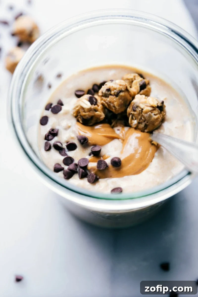 A vibrant cup of finished Peanut Butter Cookie Overnight Oats, complete with a spoon, showcasing a smooth texture and delicious mini cookie toppings, ready to be eaten.