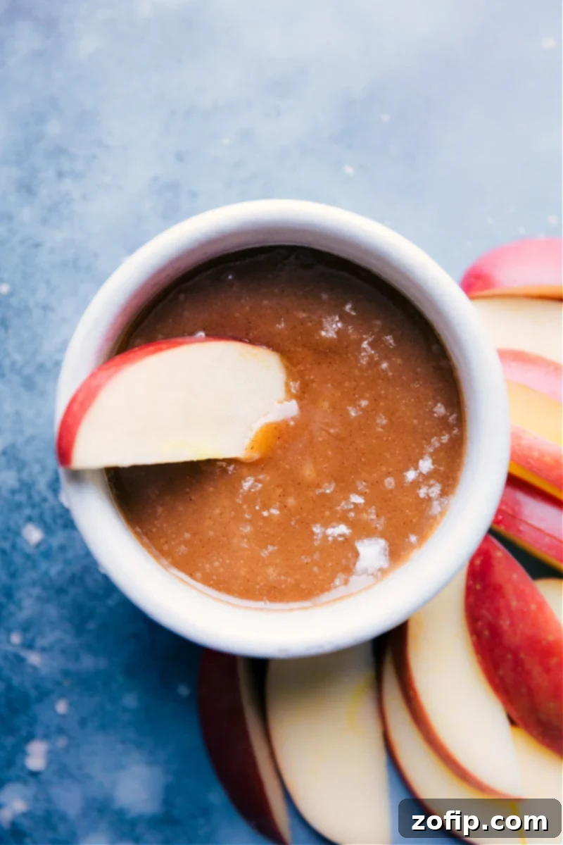 A fresh apple slice generously dipped in homemade Healthy Caramel Sauce, highlighting its smooth, decadent texture.
