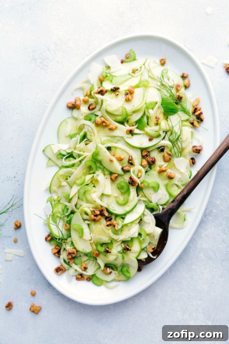 A light and tangy Apple Fennel Salad with thinly sliced apples, celery, and fennel topped with walnuts and Parmigiano Reggiano PDO Overhead shot of a vibrant Apple Fennel Salad with thinly sliced apples, celery, and fennel, garnished with toasted walnuts and shaved Parmigiano Reggiano on a white plate