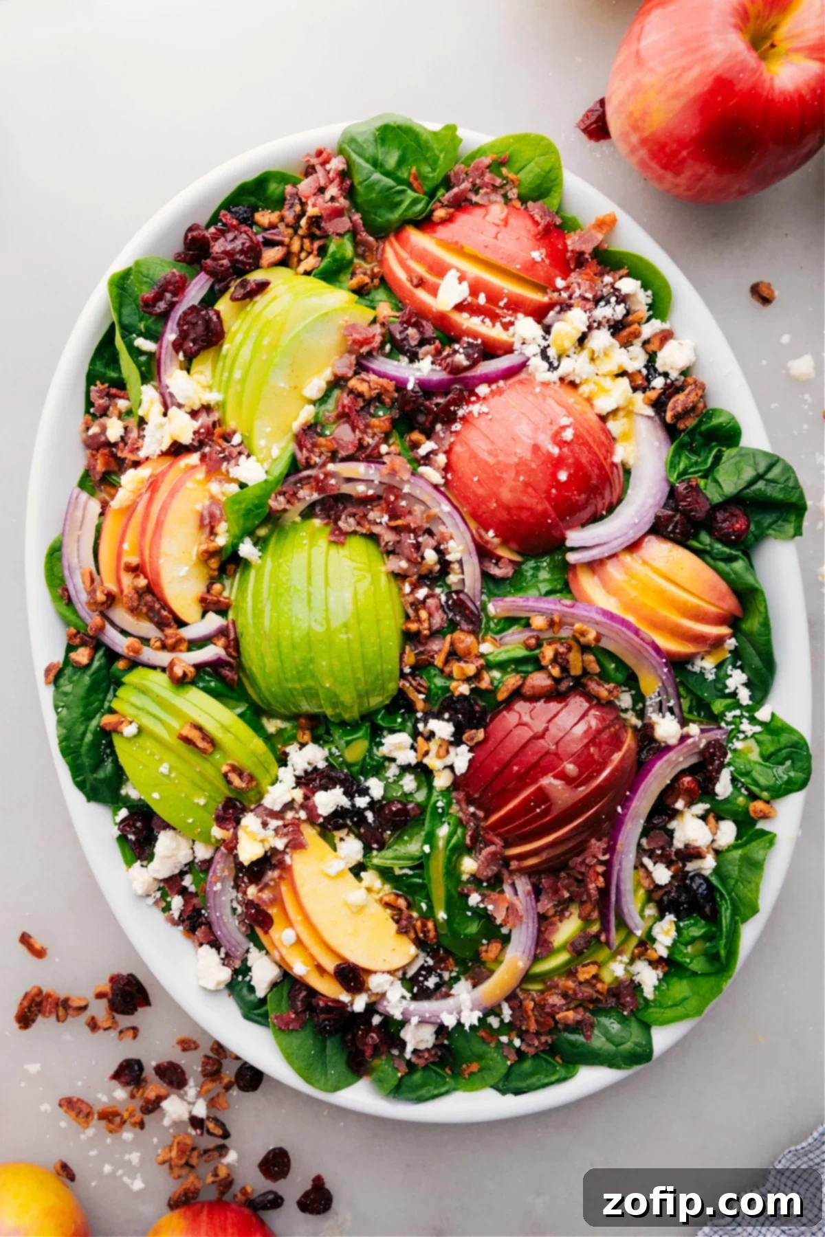A vibrant spinach salad with apples, cranberries, bacon, feta, and pecans, dressed and ready to enjoy.