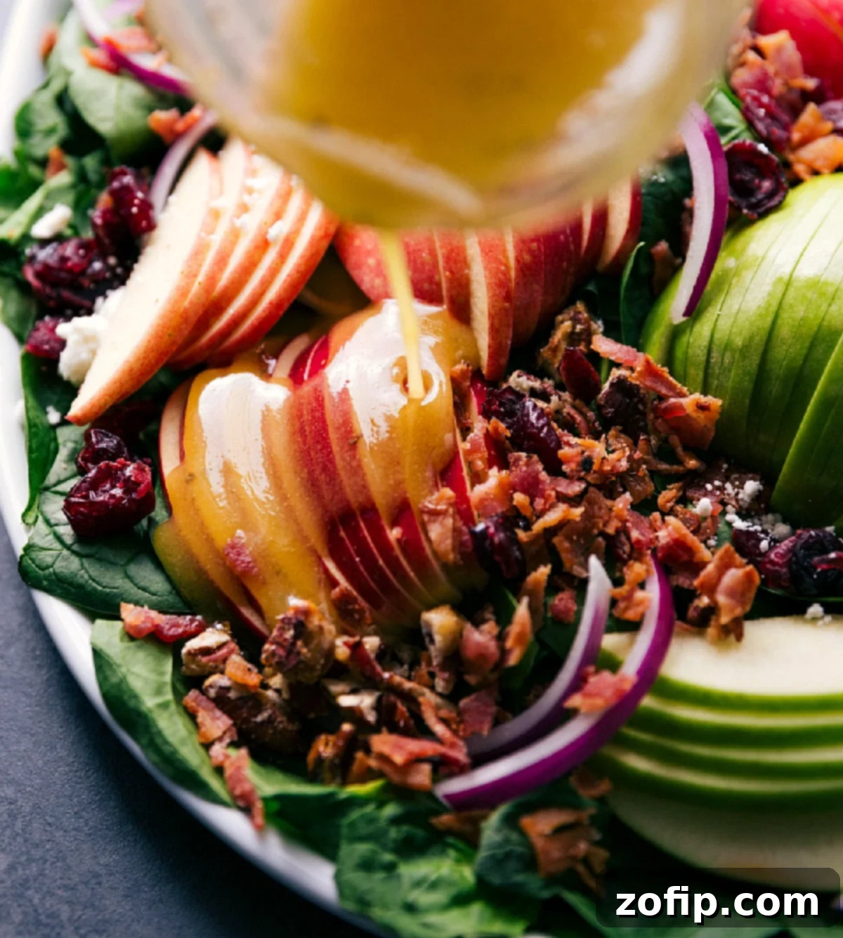 Homemade apple-Dijon vinaigrette being drizzled generously over the assembled spinach salad.