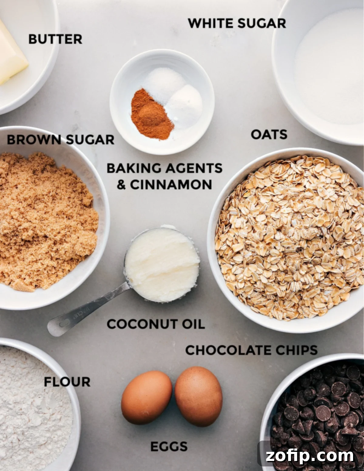 Array of ingredients for coconut oil oatmeal cookies, including oats, sugars, eggs, spices, and chocolate chips.