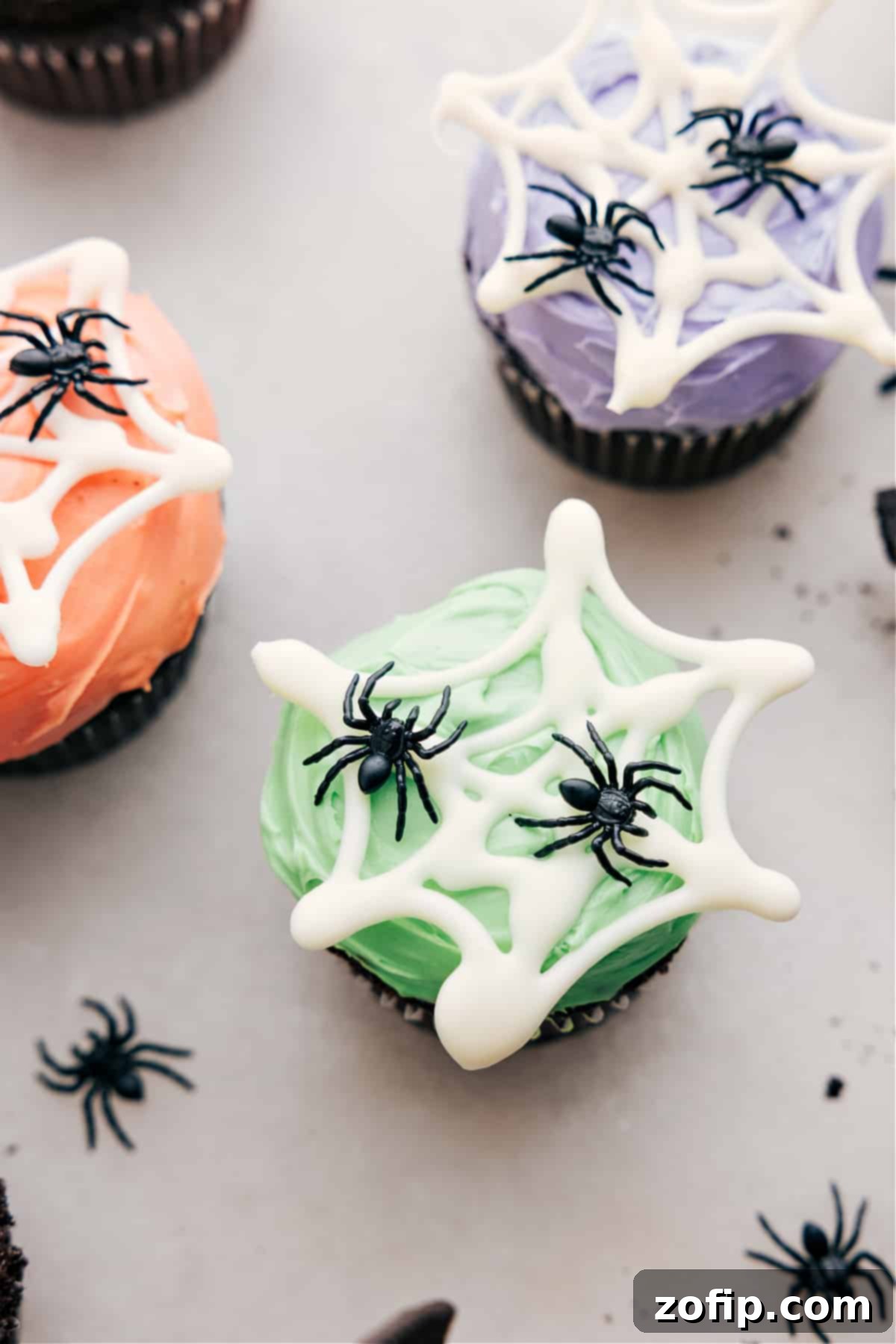 Easy And Fun Spider Cupcakes Spider web with fake spiders on colored frosting.