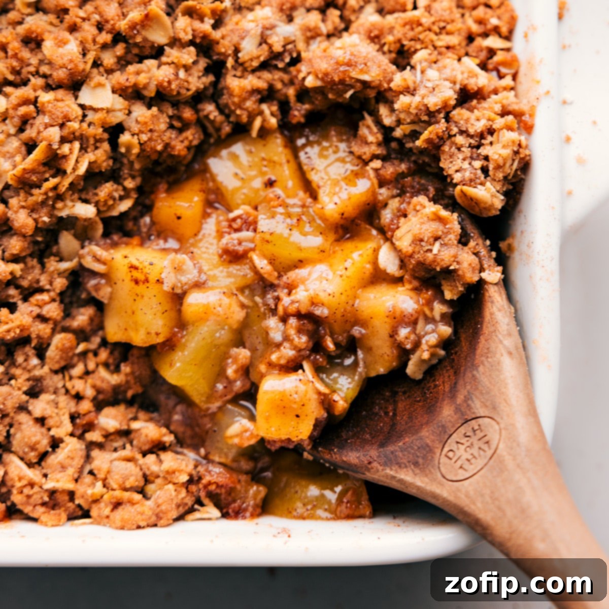 A large spoonful of warm, freshly baked apple crumble, revealing the soft cinnamon apples and crunchy oat topping, ready to be enjoyed.