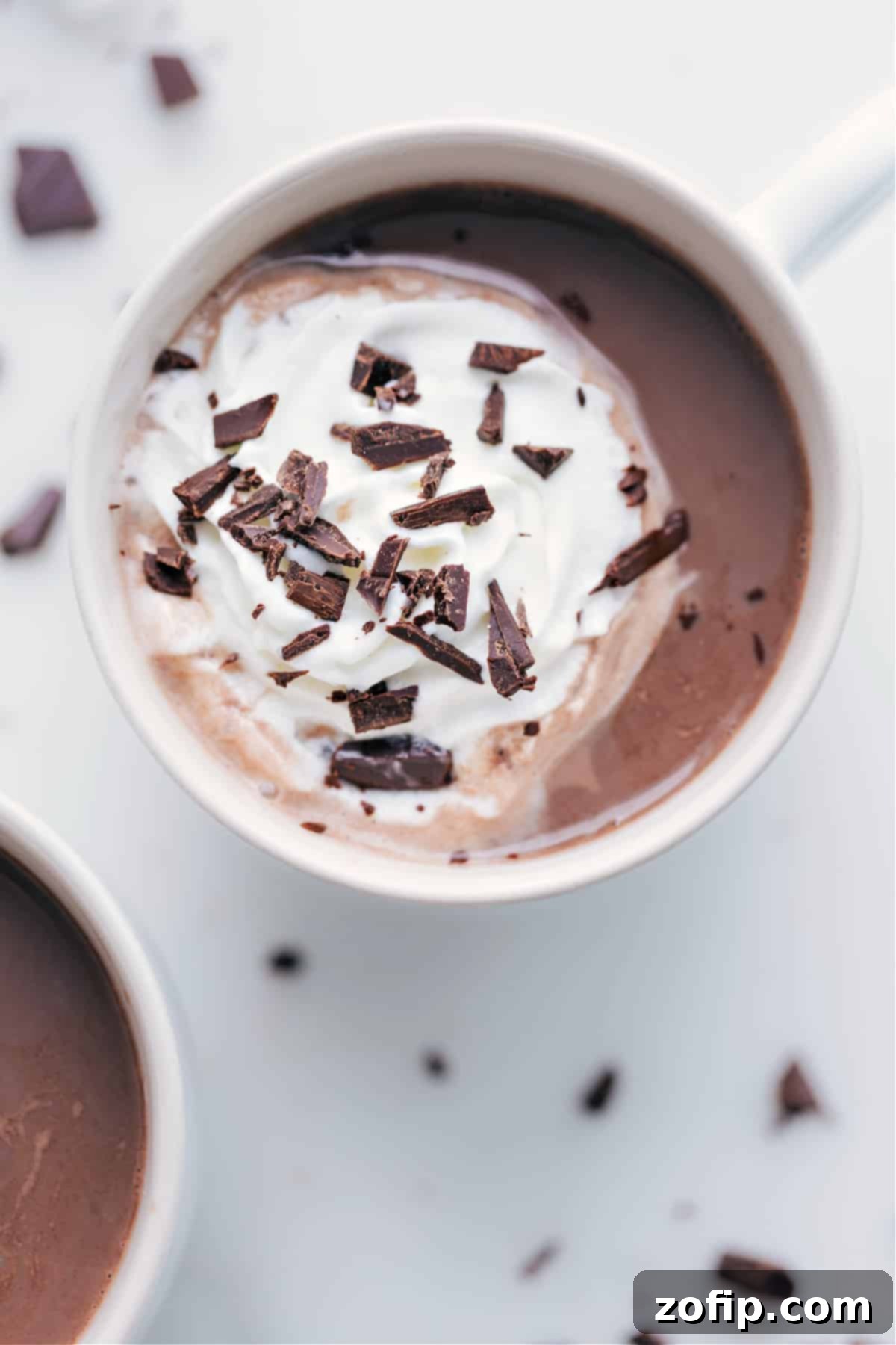 A steaming mug of rich homemade hot chocolate, generously topped with a swirl of fluffy whipped cream and delicate chocolate shavings, perfectly embodying warmth and indulgence.
