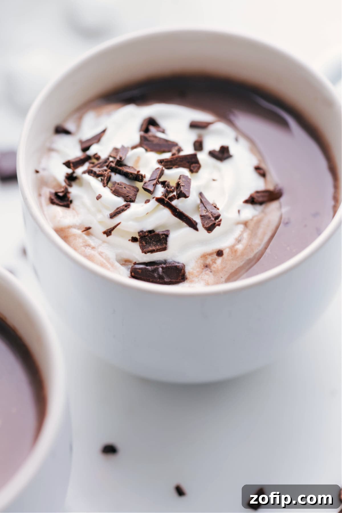 A close-up view of an inviting mug of hot chocolate, adorned with a generous dollop of whipped cream and delicate chocolate shavings, capturing the essence of indulgent comfort.