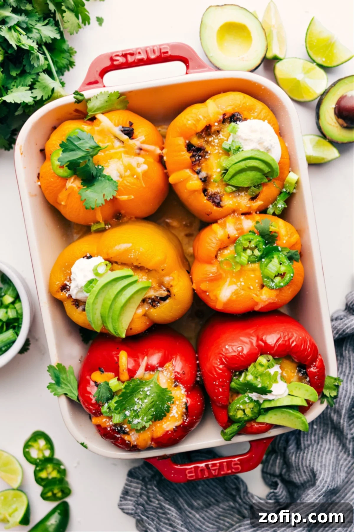 Delicious Mexican Stuffed Peppers: A Low-Carb & Protein-Packed Weeknight Dinner Idea Mexican stuffed peppers in a baking dish, generously topped with fresh cilantro, sliced jalapeños, cooling sour cream, and creamy avocado pieces.