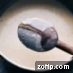 A visual guide showing the ideal consistency of the Funeral Potatoes sauce on the back of a spoon.