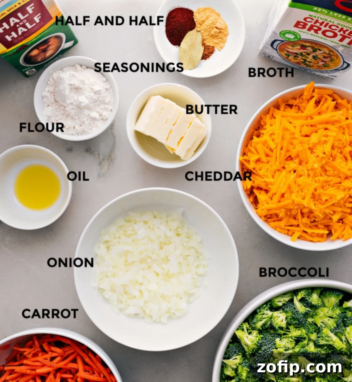 A vibrant spread of fresh ingredients including broccoli florets, shredded carrots, sharp cheddar cheese, butter, onion, garlic, spices, broth, and half-and-half, ready for soup preparation.