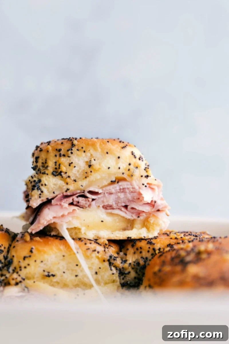 Stacked ham and cheese sliders showing the delicious melted cheese and ham inside a sweet roll.