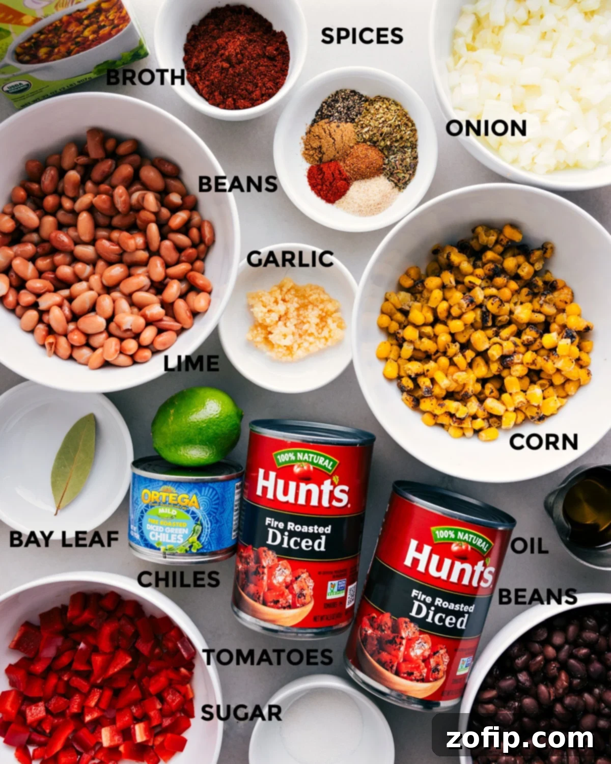 An array of fresh, colorful ingredients for vegetarian chili, including vibrant spices, chopped vegetables, assorted beans, fresh garlic, lime, vegetable broth, fire-roasted tomatoes, and green chiles, all prepped and ready for easy cooking.