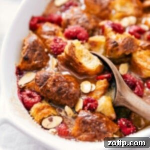 Flaky Croissant Breakfast Casserole 2 Scooping bread pudding with visible chunks of bread, drizzled syrup, and fruit pieces.