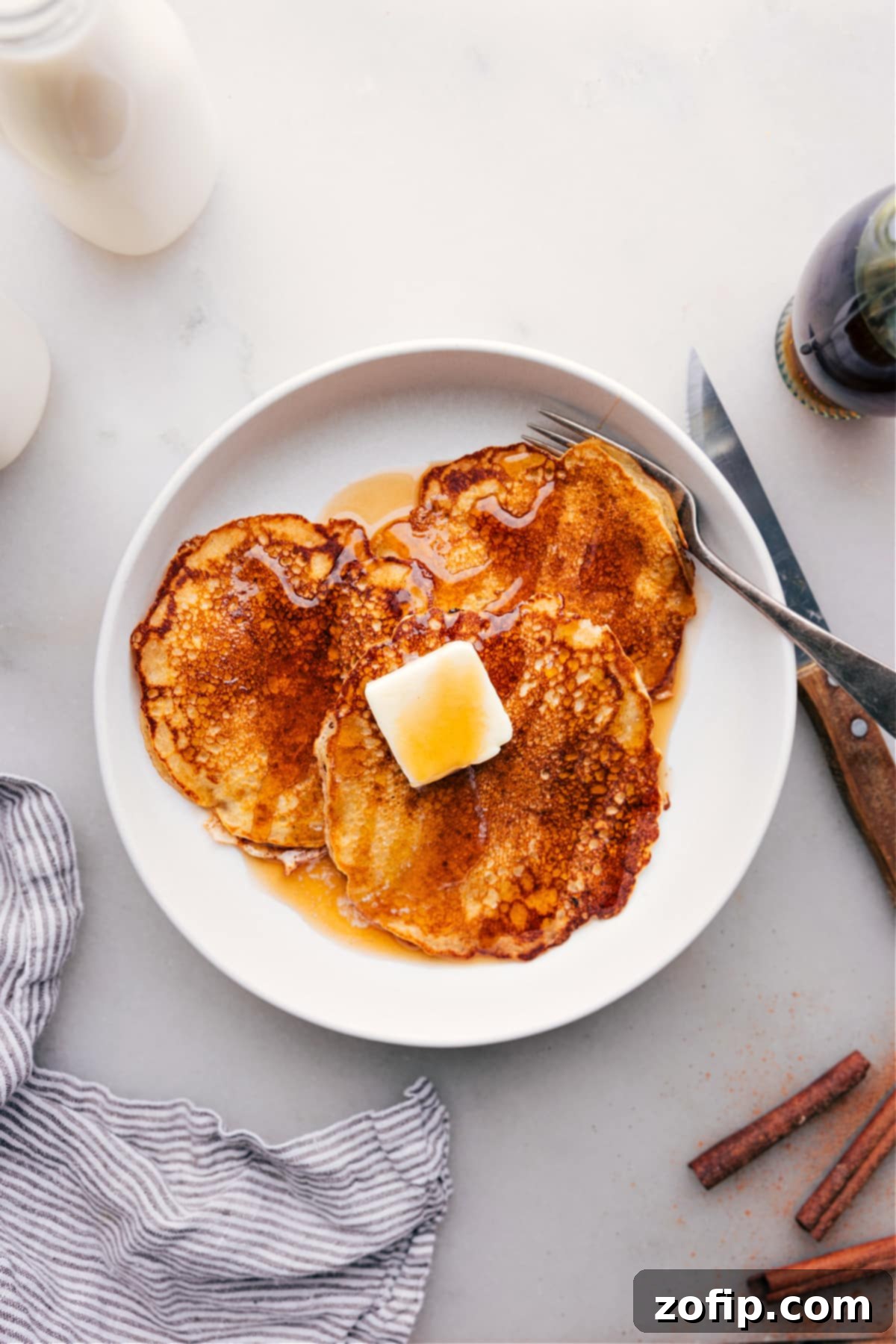 Sumptuous Pancake Stack with Syrup A sumptuous stack of golden Old-Fashioned Pancakes, generously drizzled with rich maple syrup, resting on a pristine white plate, promising a delightful breakfast.