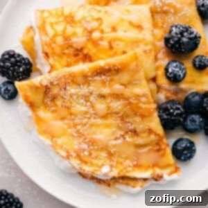 Plate of three crepes with berries and syrup drizzled on top.