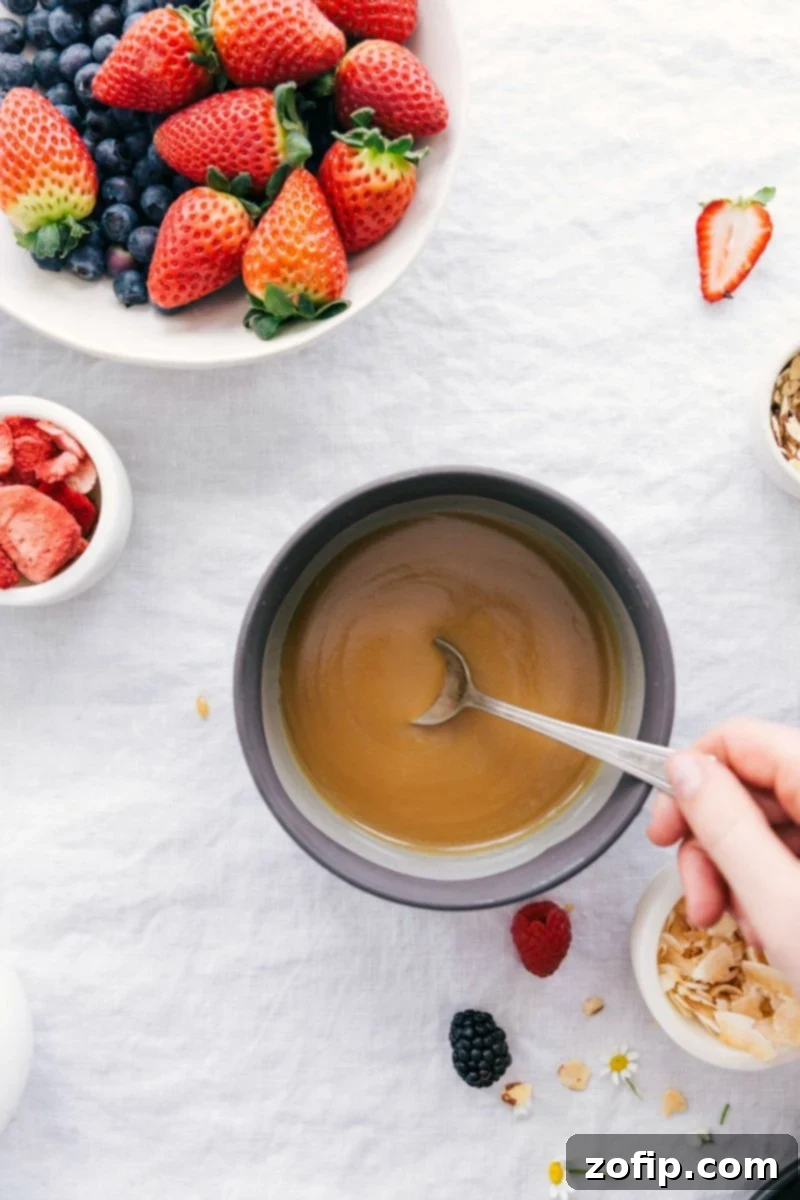 Overhead photo of a creamy vanilla sauce in a decorative bowl, surrounded by fresh red and blue berries, suggesting a delightful topping for various dishes. The sauce is smooth and glistening.
